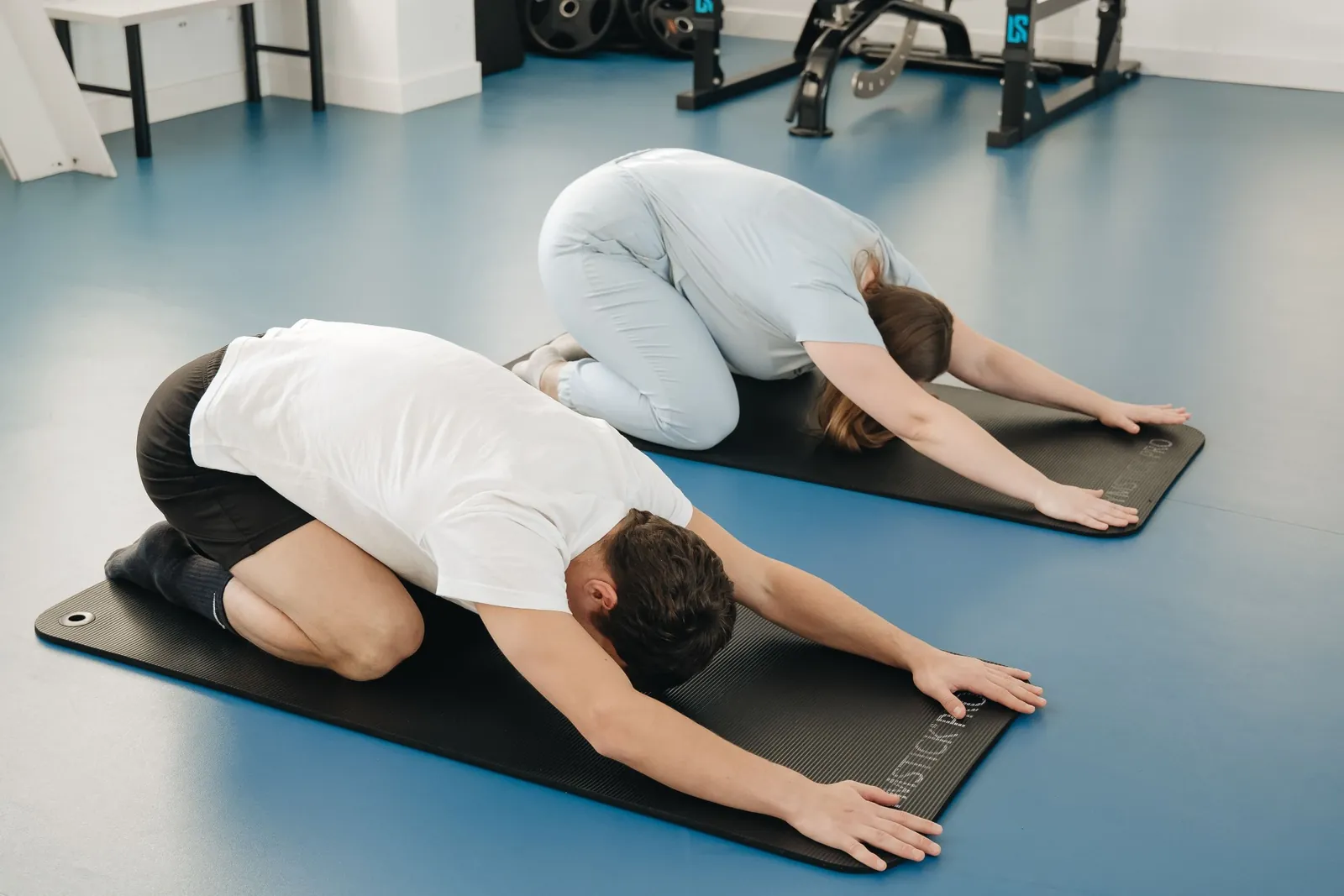 Therapist and athlete doing a guided child's pose stretch on mats